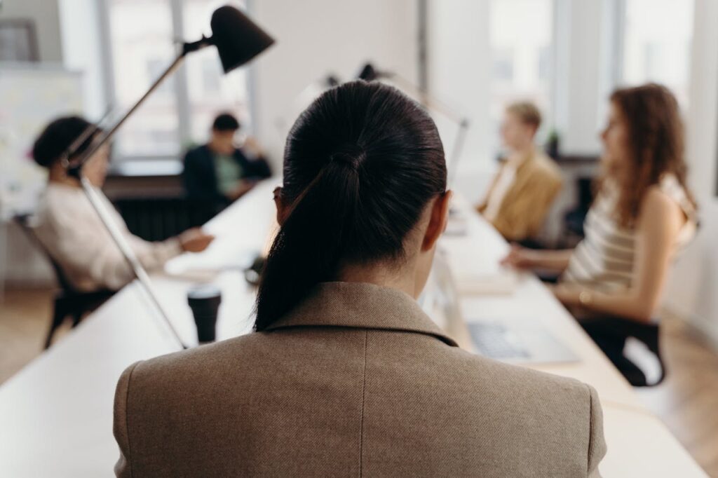 Office team collaborating in a modern workspace, viewed from behind a female employee.