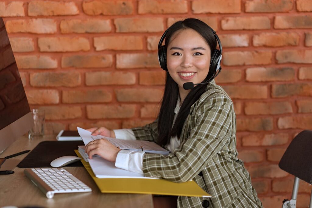 Filipina call center agent smiling at her desk with a headset in a BPO office.