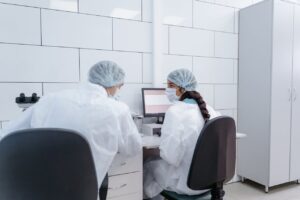 Two lab technicians in protective gear analyzing data on a computer, representing scientific research and healthcare analysis.