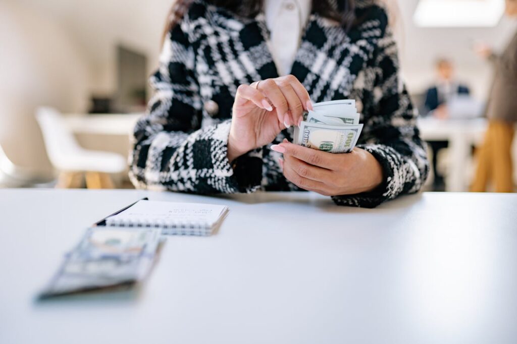 A businesswoman counting US dollar bills at her office desk, representing financial planning and business management.