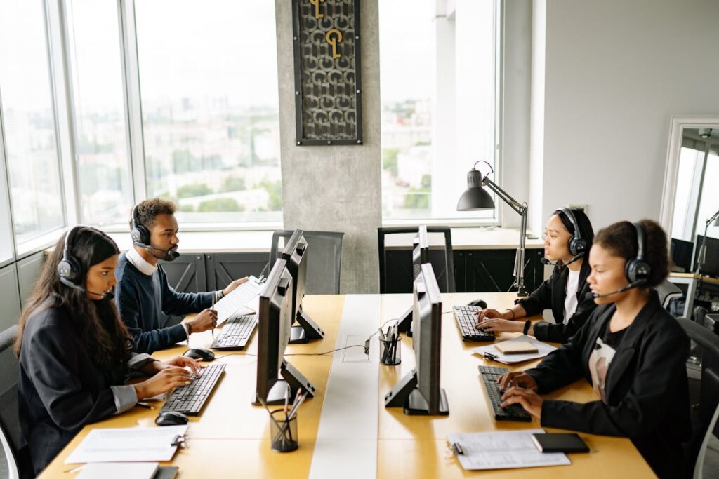 A diverse team of customer service representatives in a modern office, handling inquiries using headsets and computers.