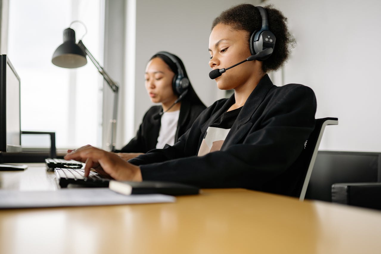 Two customer service representatives wearing headsets and working on computers in a modern call center, providing support and assistance.