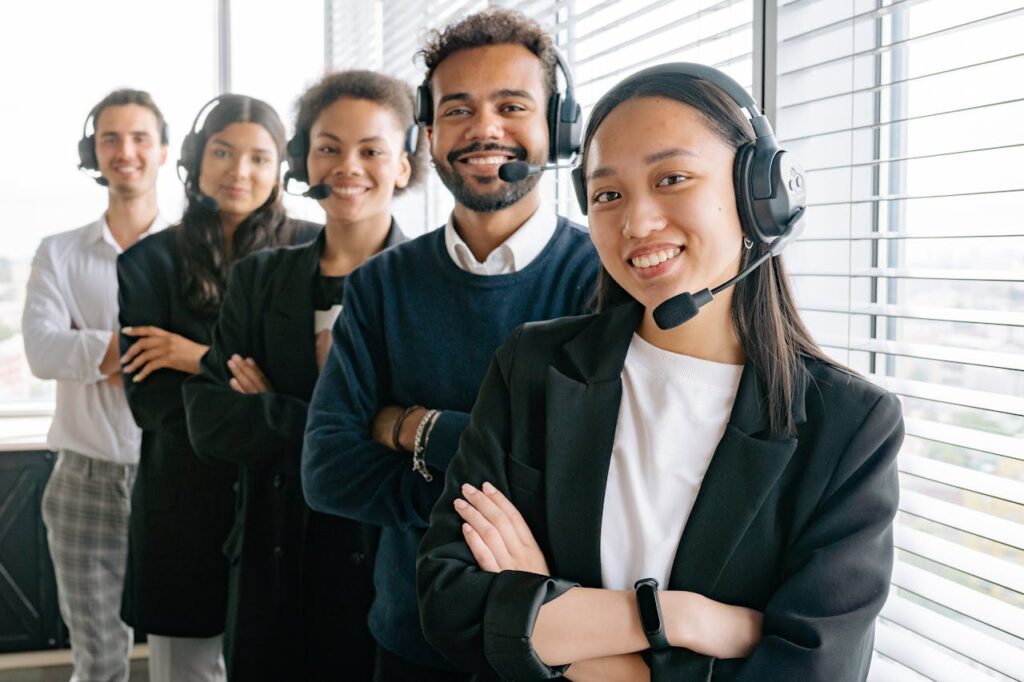 Diverse group of call center agents wearing headsets, standing confidently in an office.