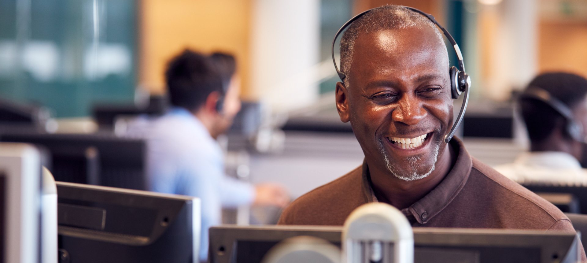 Smiling back-office operations specialist with a headset working at his desk in a busy operations center, representing back-office outsourcing in the Philippines