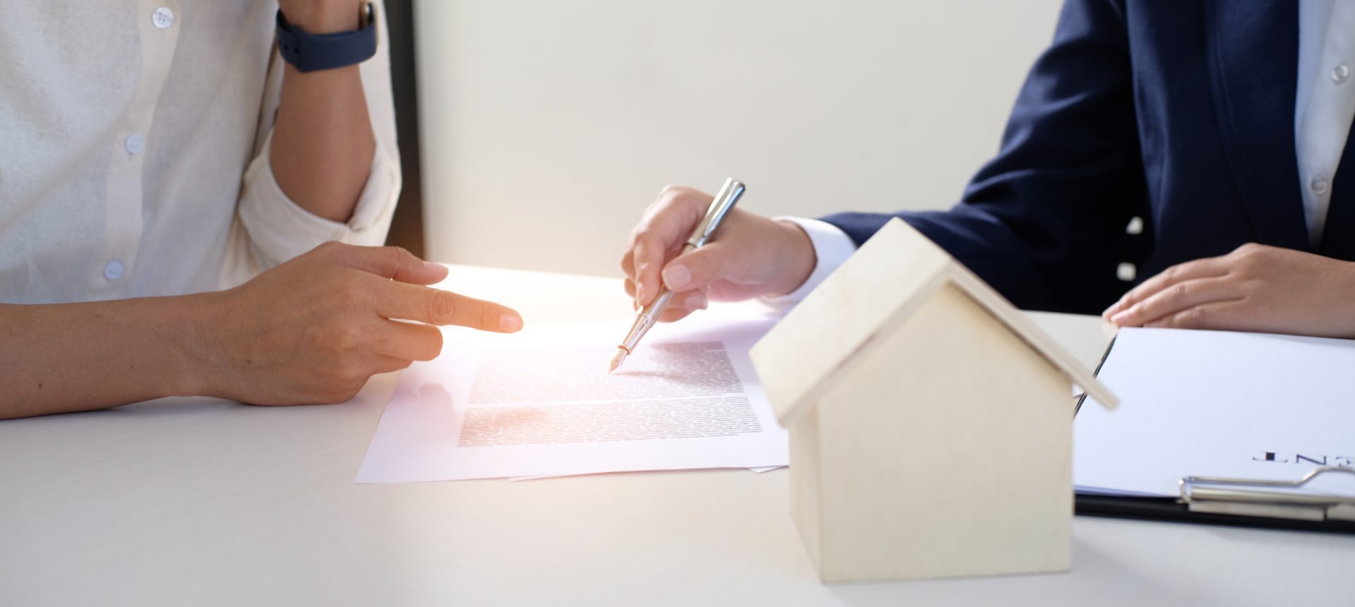 Adjuster pointing a pen at a claim form beside a model house while a homeowner reads along after a catastrophe