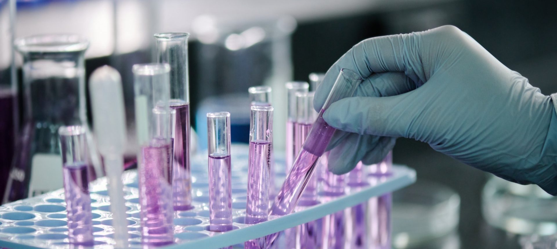 Gloved hand placing a test tube in a rack, the sample handling that clinical trial operations track