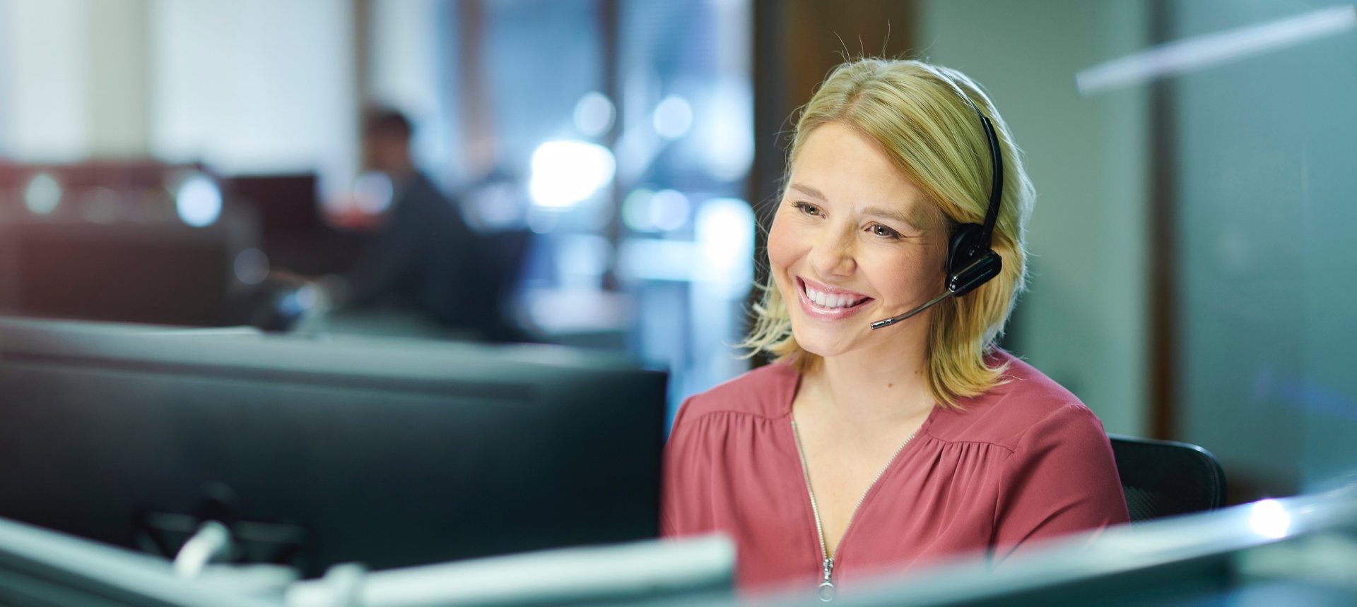 Smiling customer service agent with a headset helping a customer at her workstation, representing customer service outsourcing in the Philippines