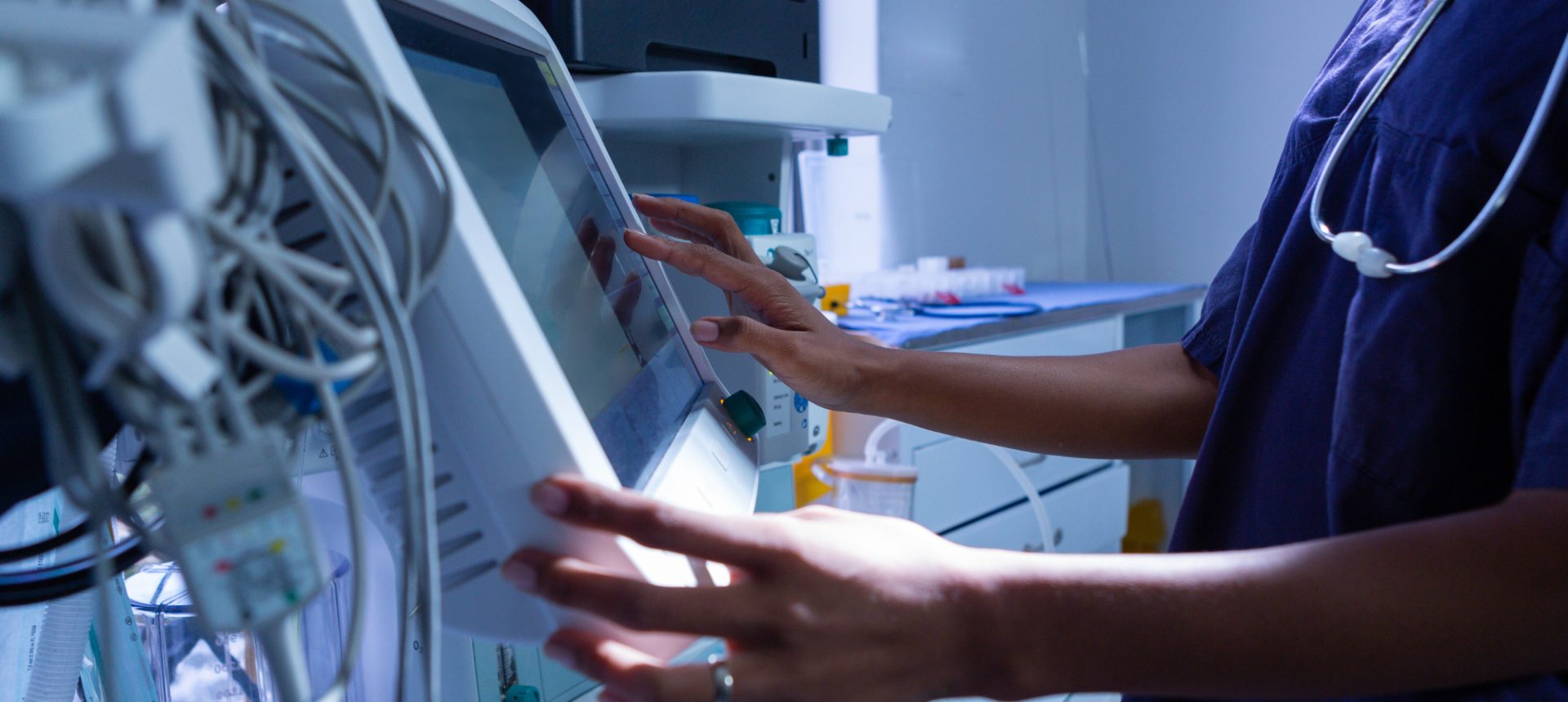 Nurse in scrubs setting a ventilator's touch screen, the kind of durable medical equipment that is ordered and billed