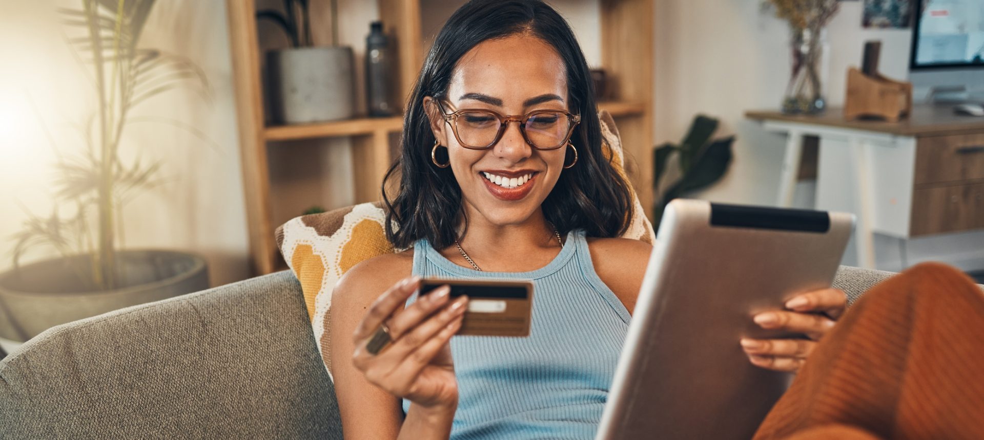 Smiling woman on a sofa shopping online with a tablet and a credit card, for e-commerce