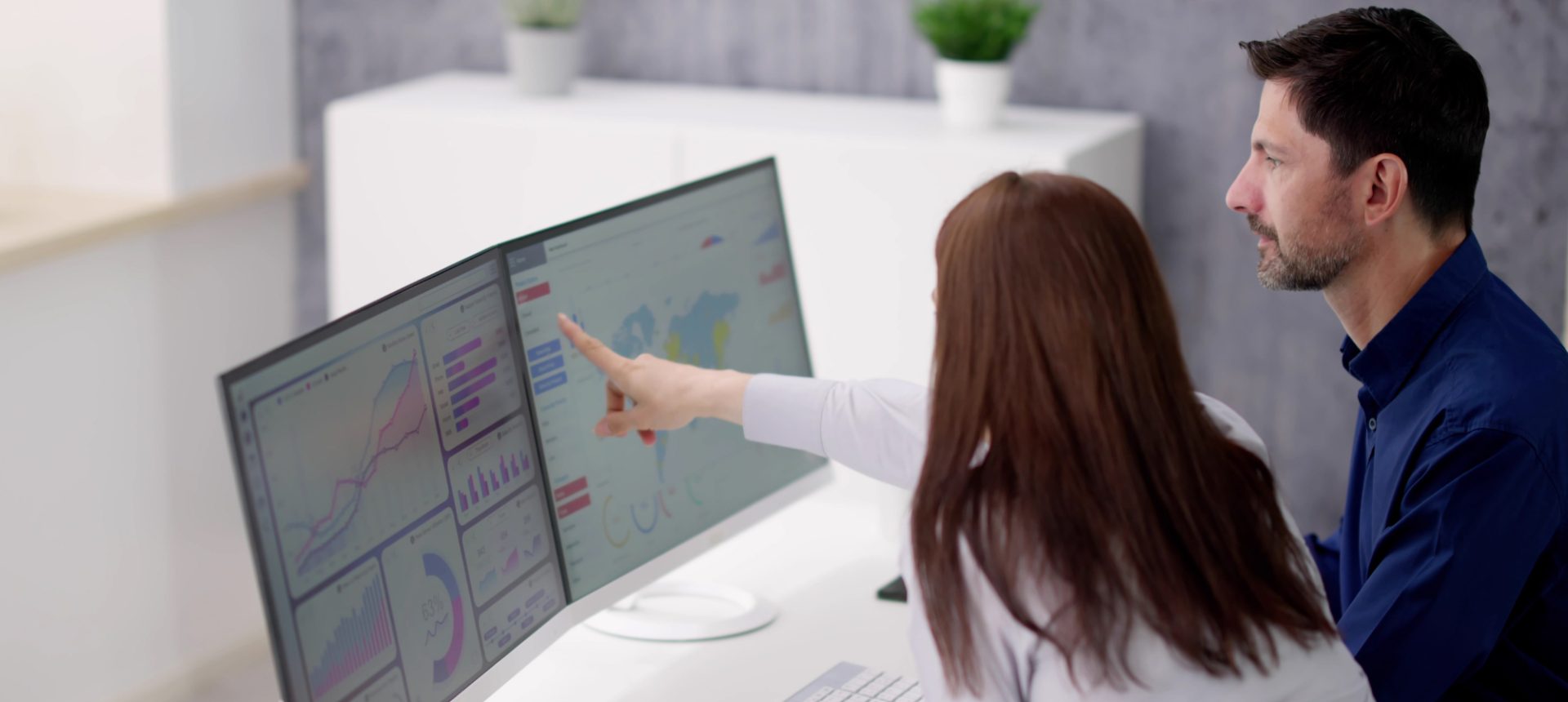 Analyst pointing at a dashboard on twin monitors while a colleague follows, reviewing first-person capture data