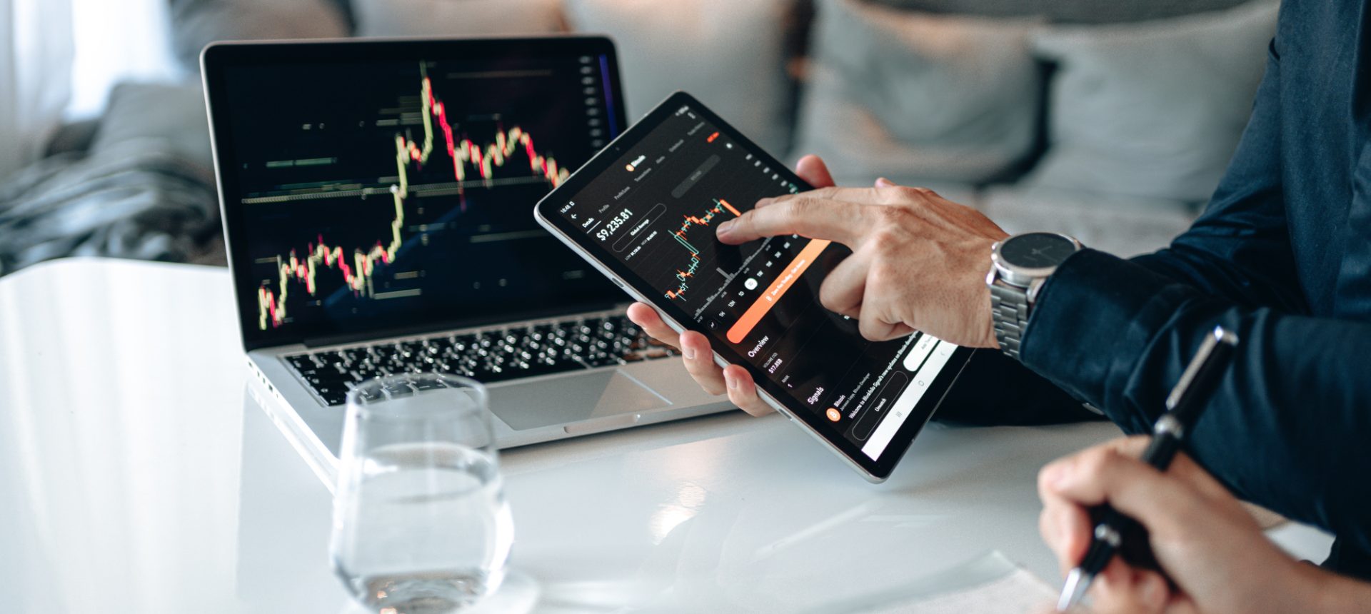 Hand tapping a price chart on a tablet beside a laptop of market data, the in-app finance an embedded finance team runs