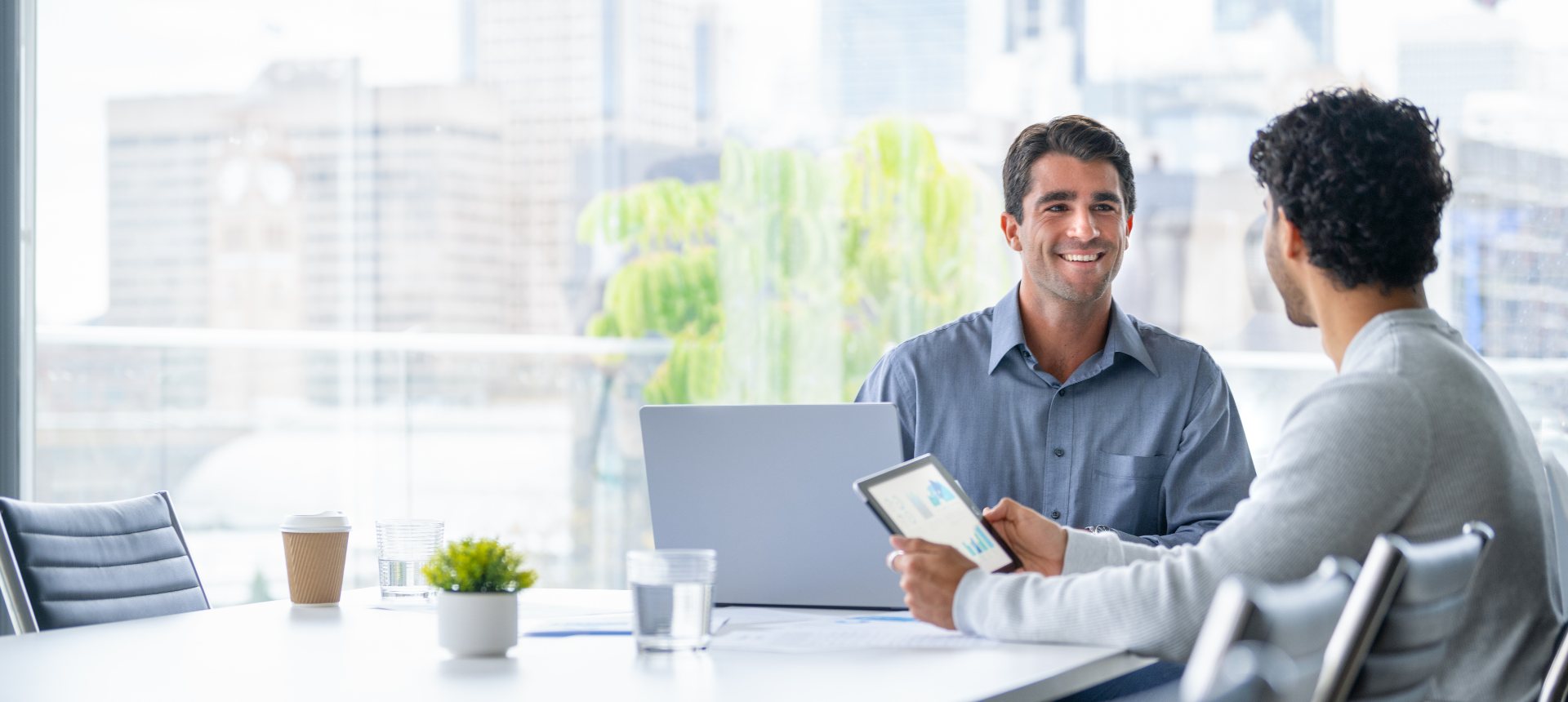 Smiling fintech product lead reviewing a dashboard on a tablet with a colleague in a city-view meeting room