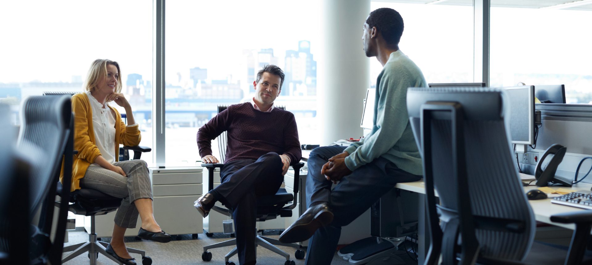 Three colleagues talking between desks in a bright office, the claims team that picks up a first notice of loss