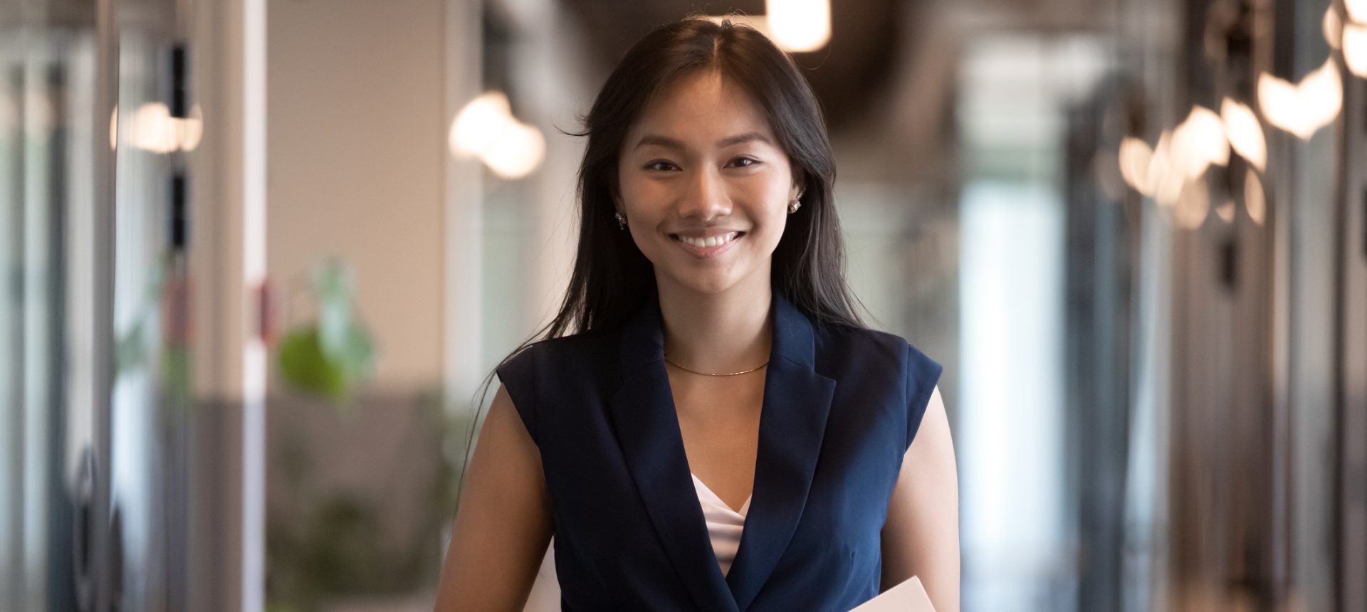 Smiling hotel guest-services professional holding documents in a bright hotel corridor