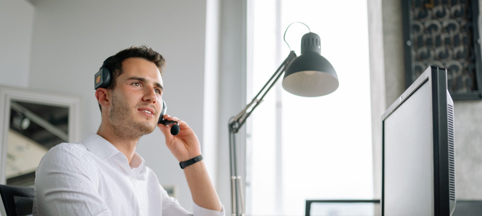 Intake specialist adjusting his headset at a desk monitor, taking a prospective client's call for a law firm