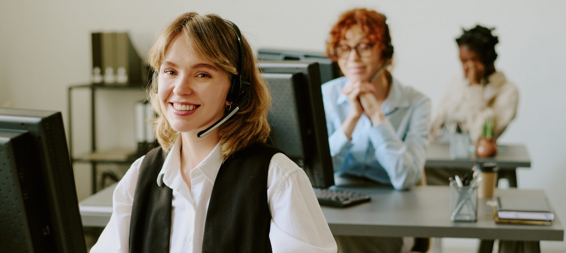Smiling reviewer with a headset at her desk on a quiet verification floor, clearing referred sign-ups