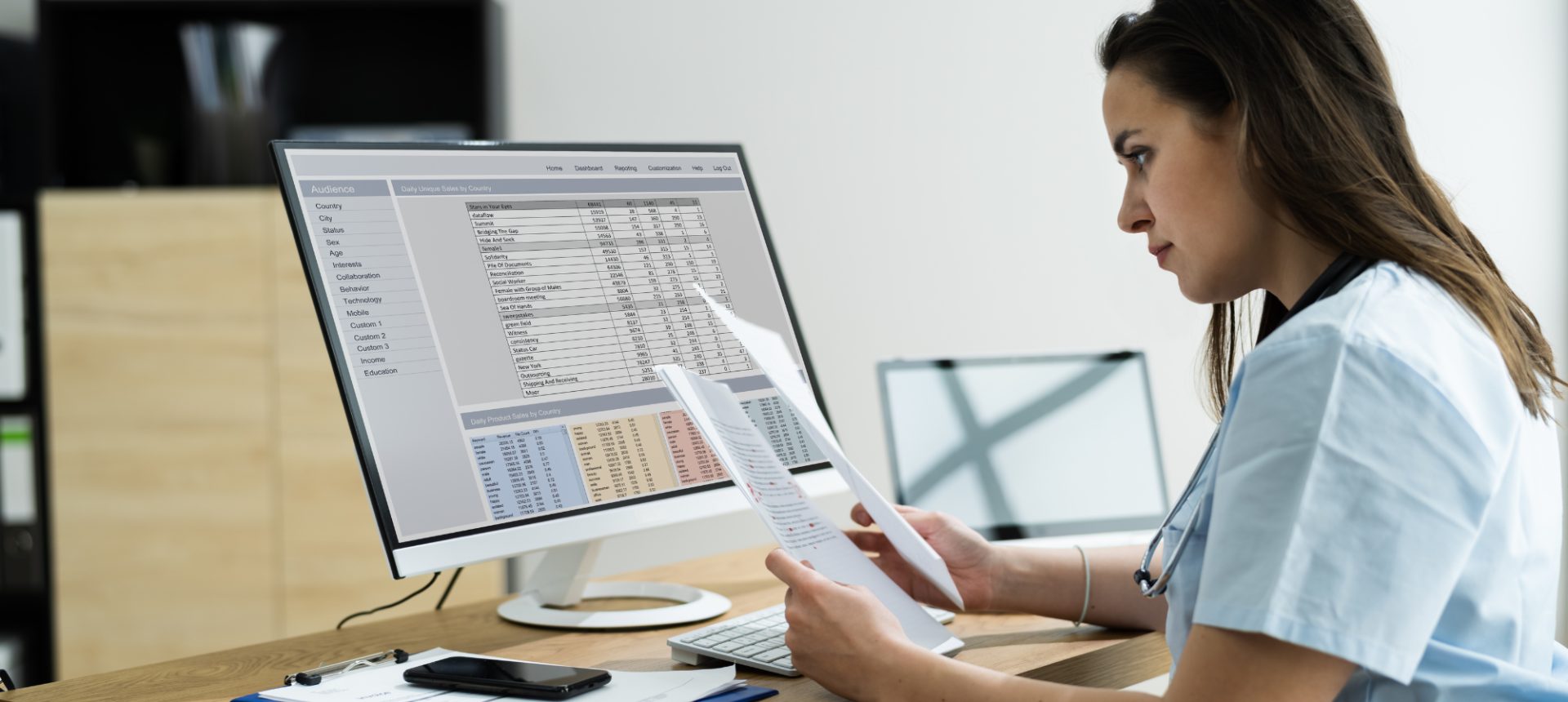 Clinical annotator in scrubs checking a chart against labeled fields on her monitor