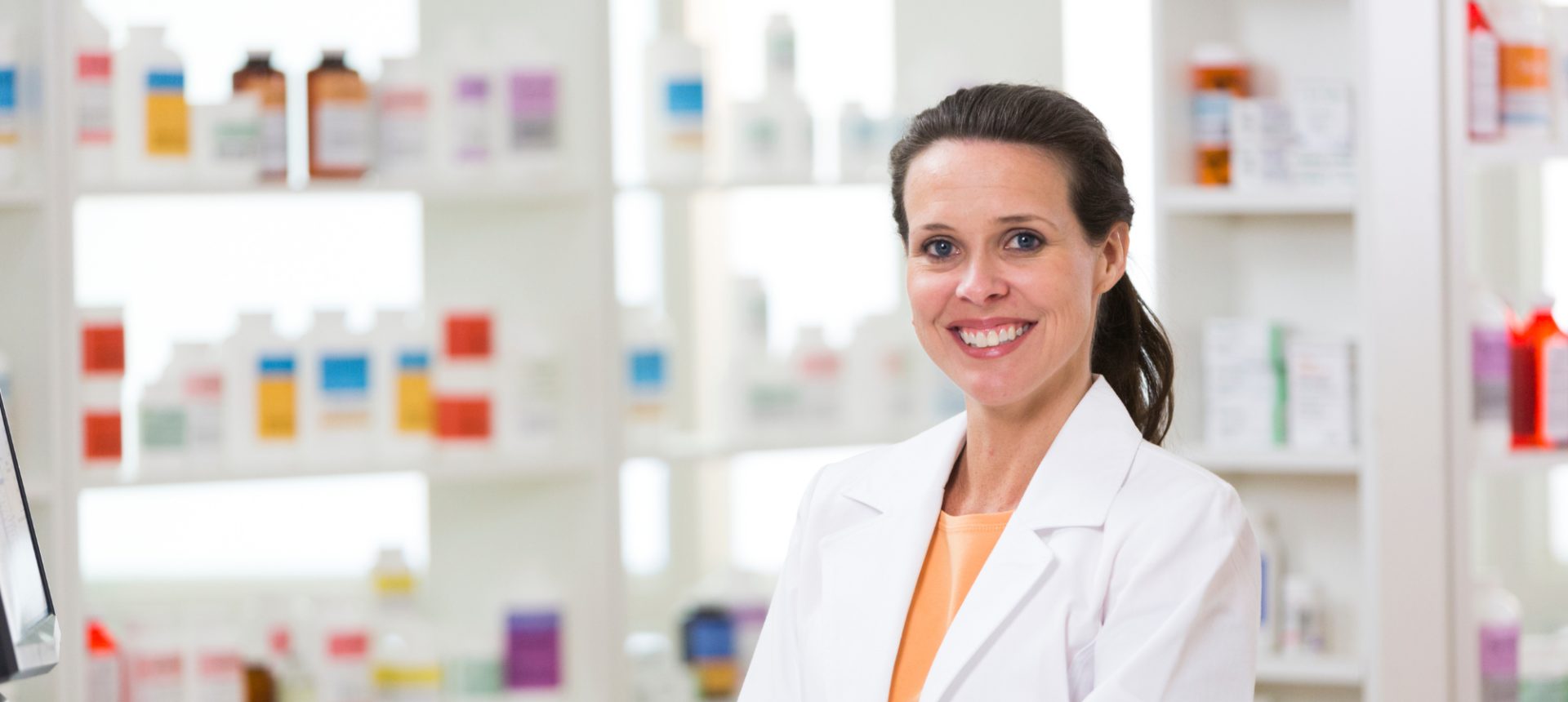 Smiling pharmacist holding a medicine bottle at the counter, where many adverse event reports for pharmacovigilance begin
