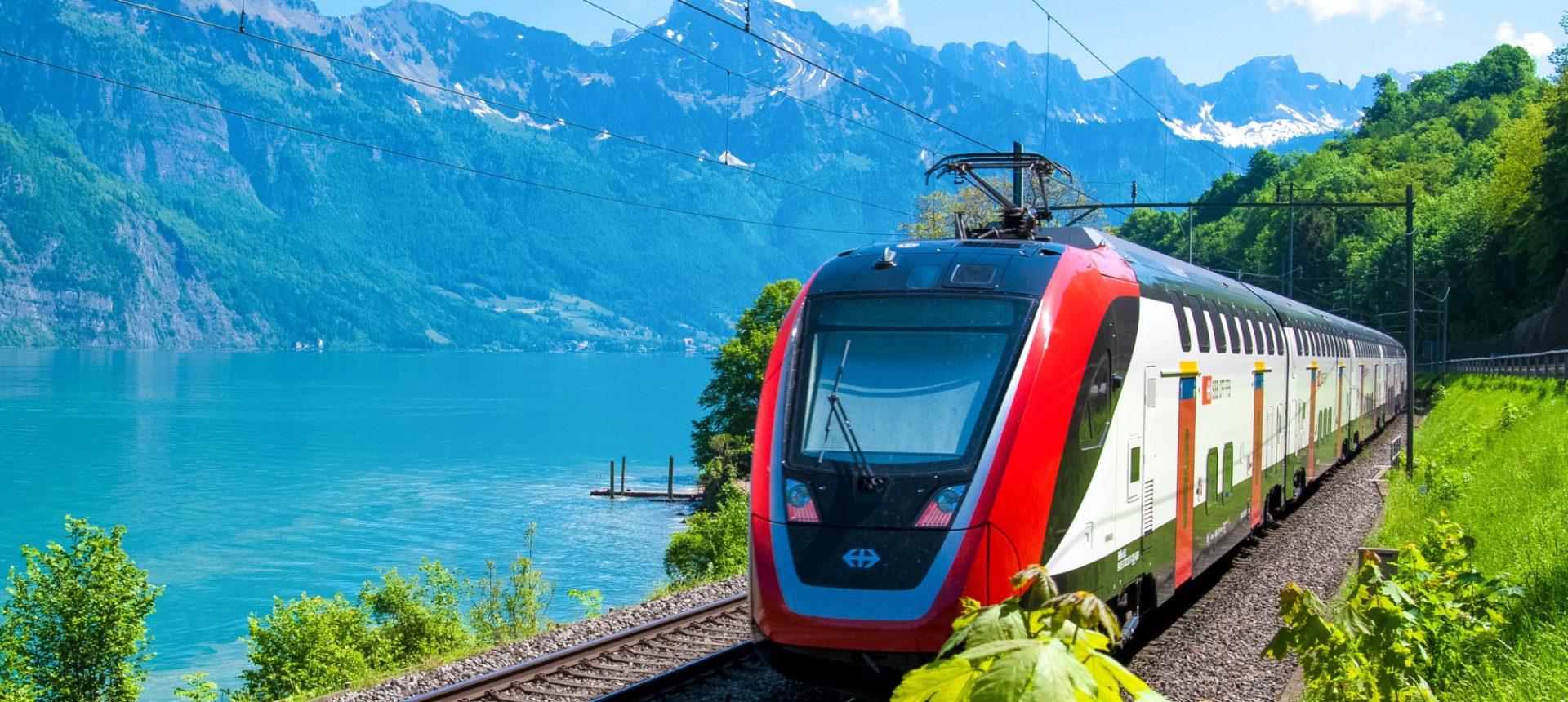 Red passenger train running along a mountain lake, the rail journeys a multi-modal travel support desk rebooks