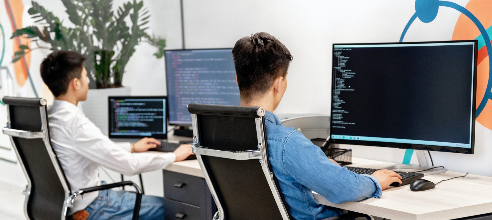 Two developers writing code at dual-monitor workstations in a software office