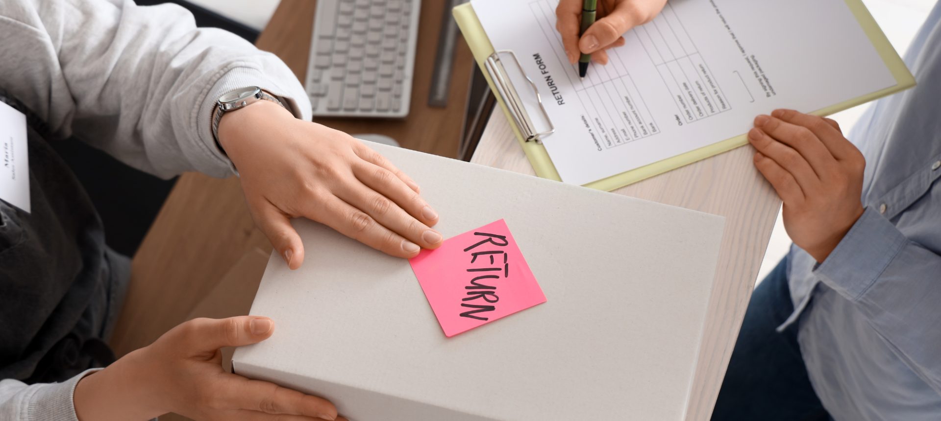 Box tagged with a pink return note handed over as a return form is filled in, the exchange a fit returns team processes