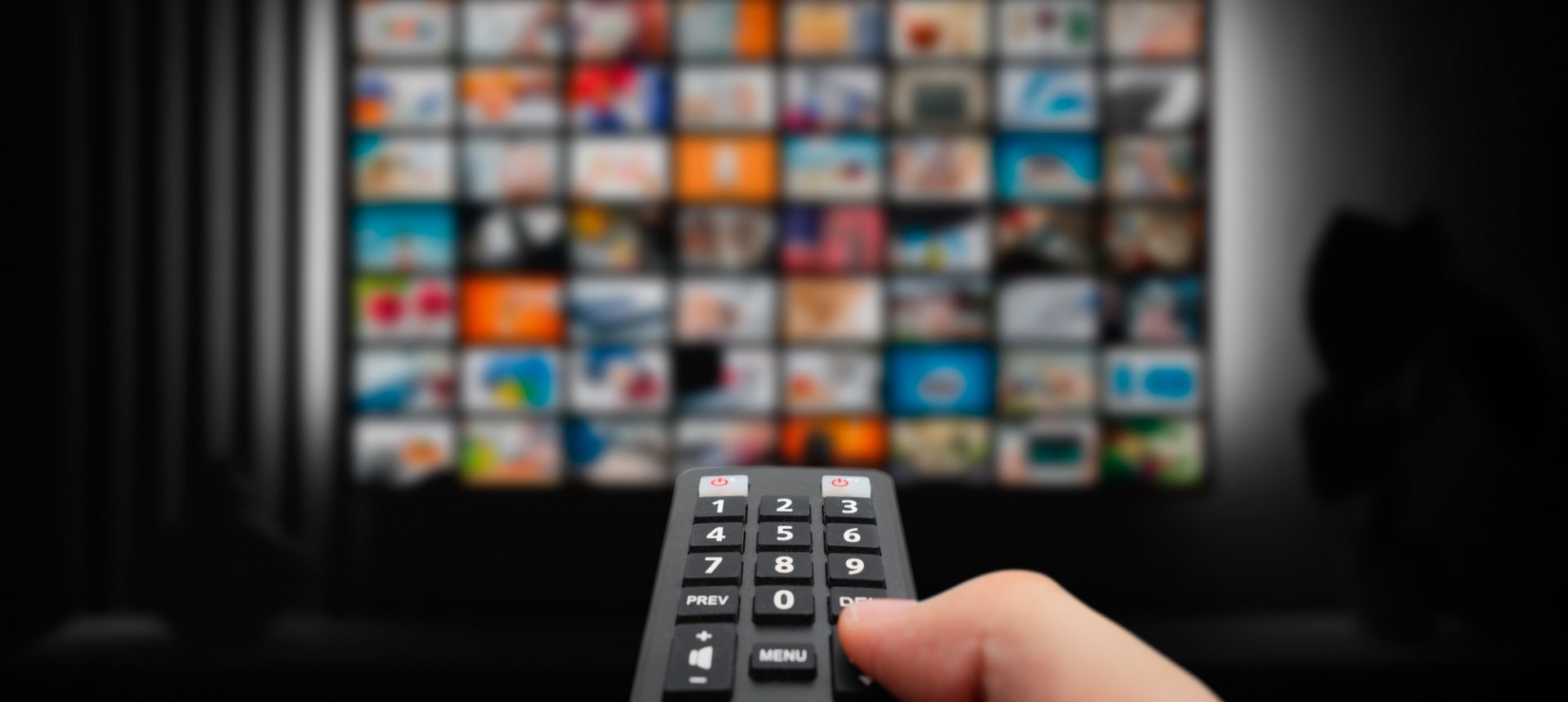 Hand aiming a remote at a wall of streaming titles, the subscription a replenishment operations team keeps running