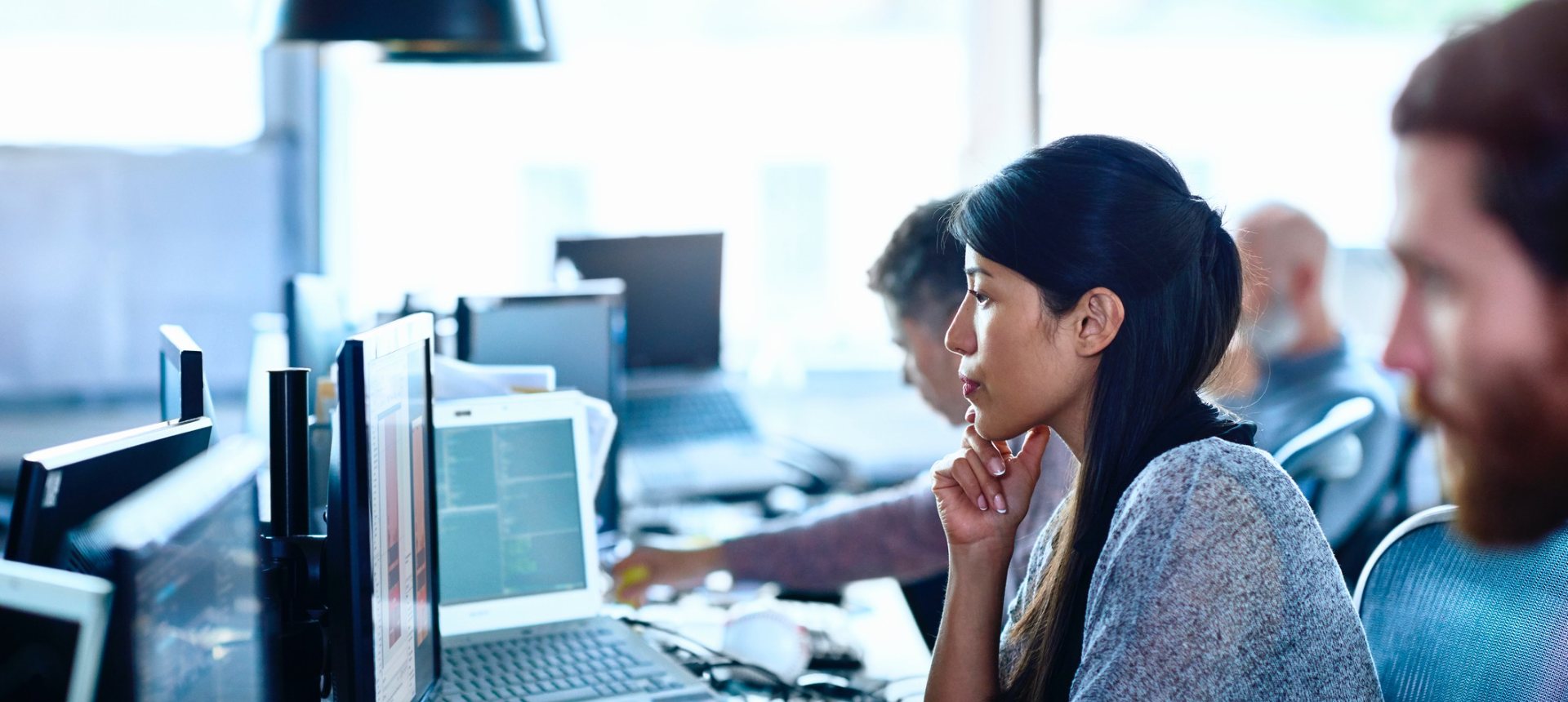 Technical support engineer studying a troubleshooting screen in an open-plan support office, representing technical support outsourcing in the Philippines