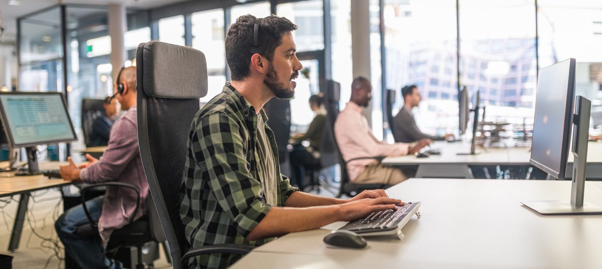 Support agent wearing a headset typing at a workstation in a busy open-plan technology support office, representing technology outsourcing in the Philippines