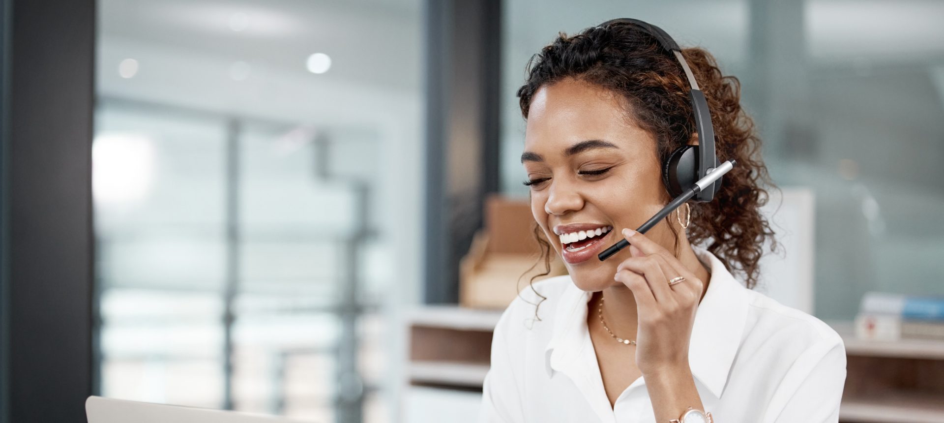 Smiling customer support agent with a headset helping a subscriber on a call at her laptop, for telecommunications