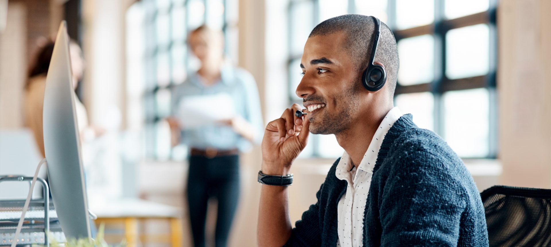 Smiling guest services agent with a headset talking a traveler through a booking change at his computer
