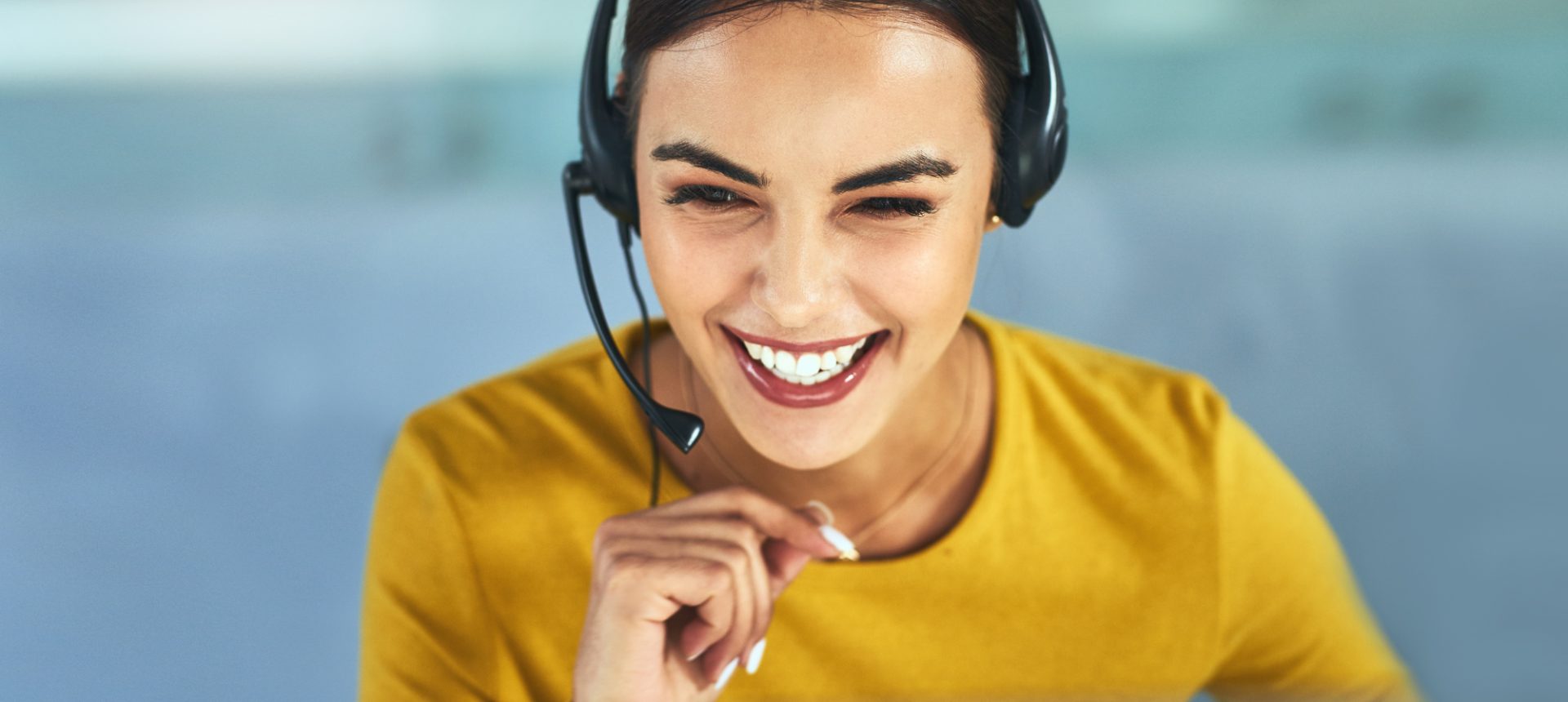 Smiling care agent in a yellow top with a headset laughing with a customer on the phone