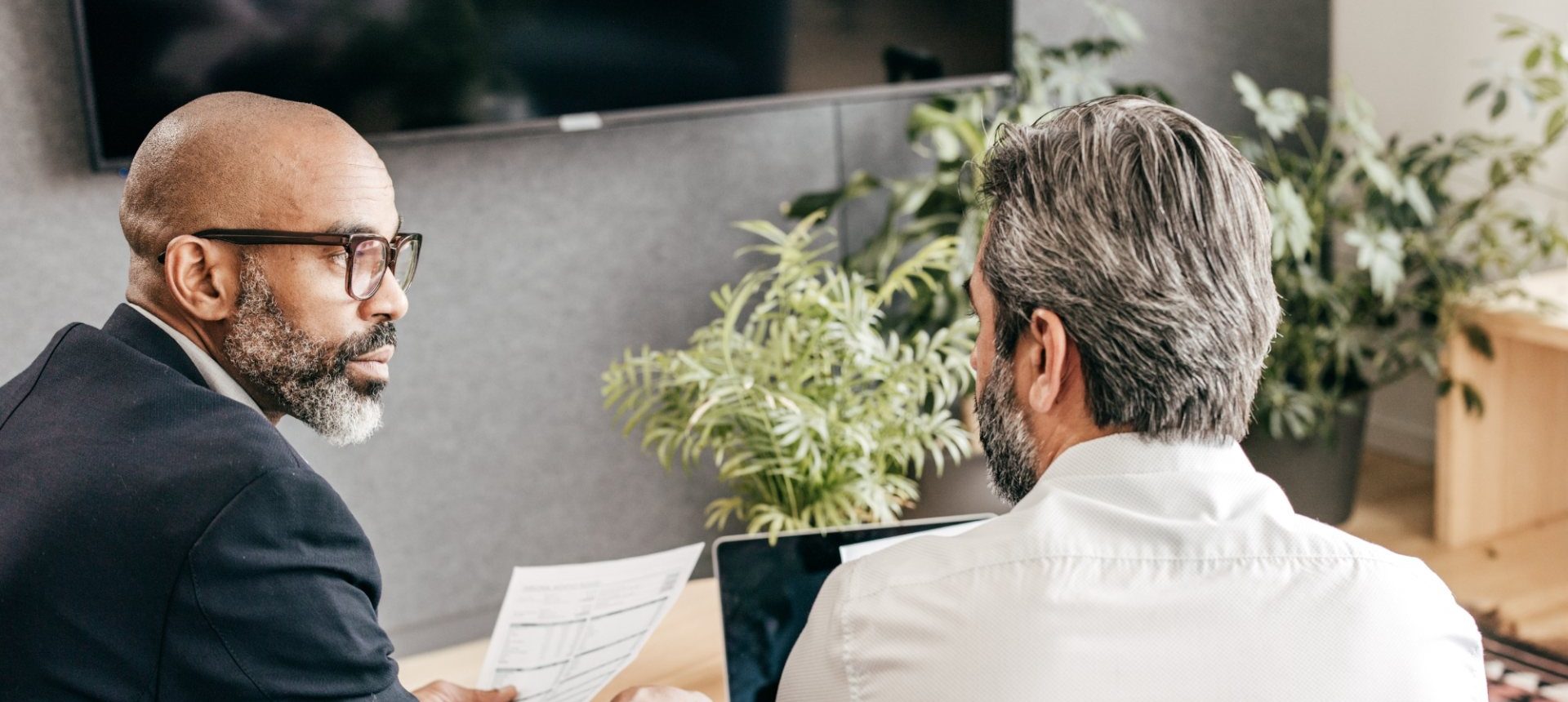 Two advisors reviewing a client document at a laptop, the paperwork a wealth management service team prepares