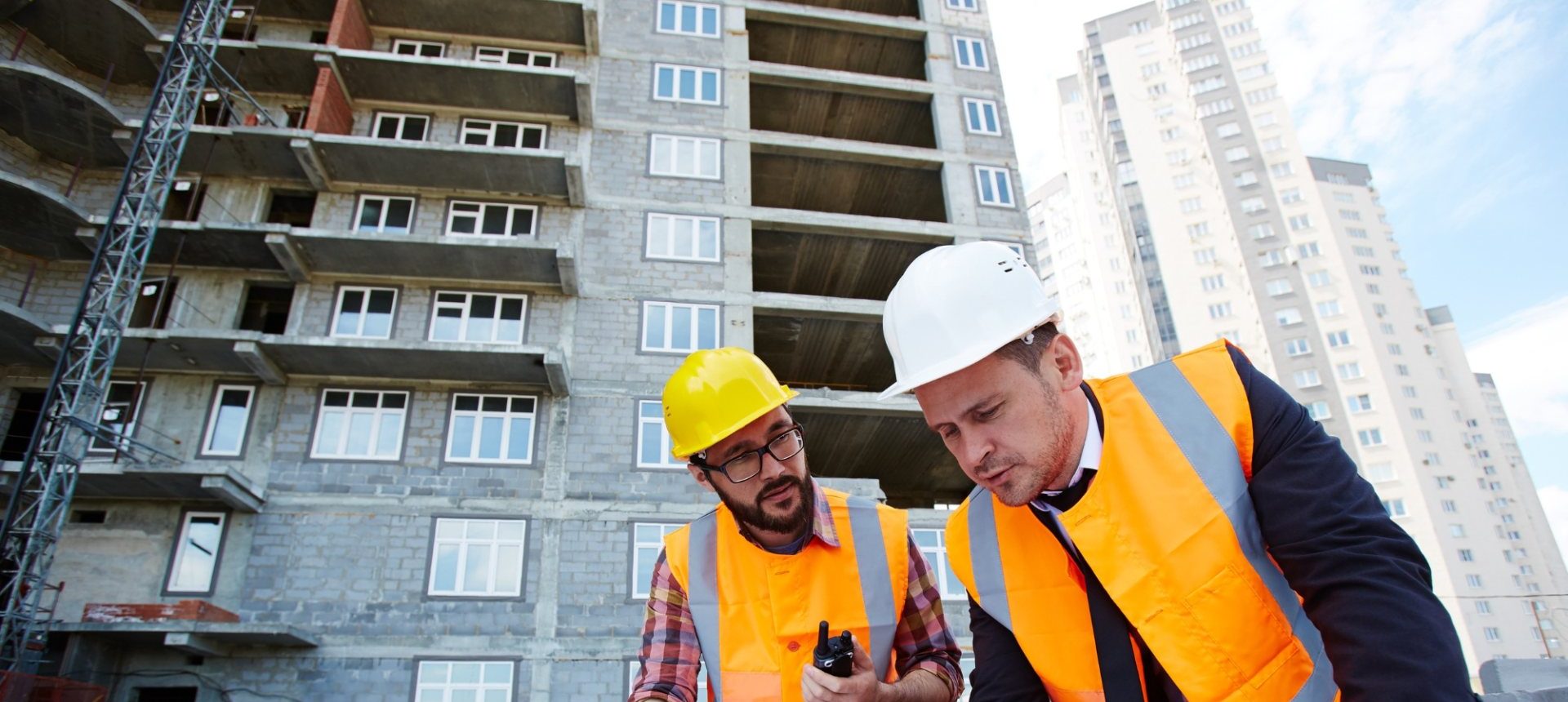 Two site supervisors in safety vests reviewing plans, the workplace injury setting behind workers' comp billing