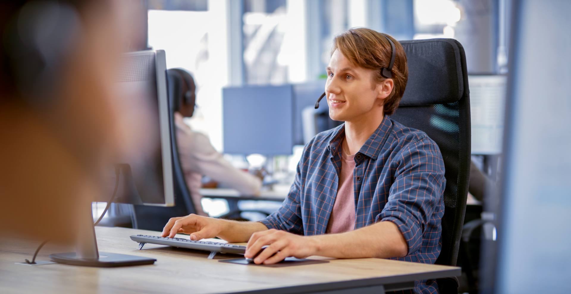 Call center agent with a headset at his desk, working alongside AI voice and chat tools
