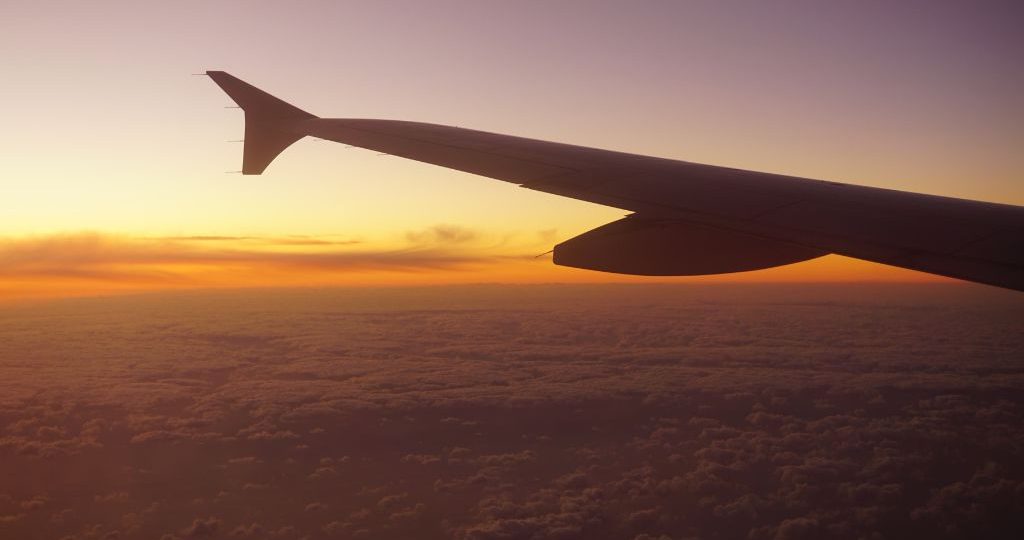 Airliner wing above the clouds at sunset from a cabin window, the passenger journey aviation support looks after