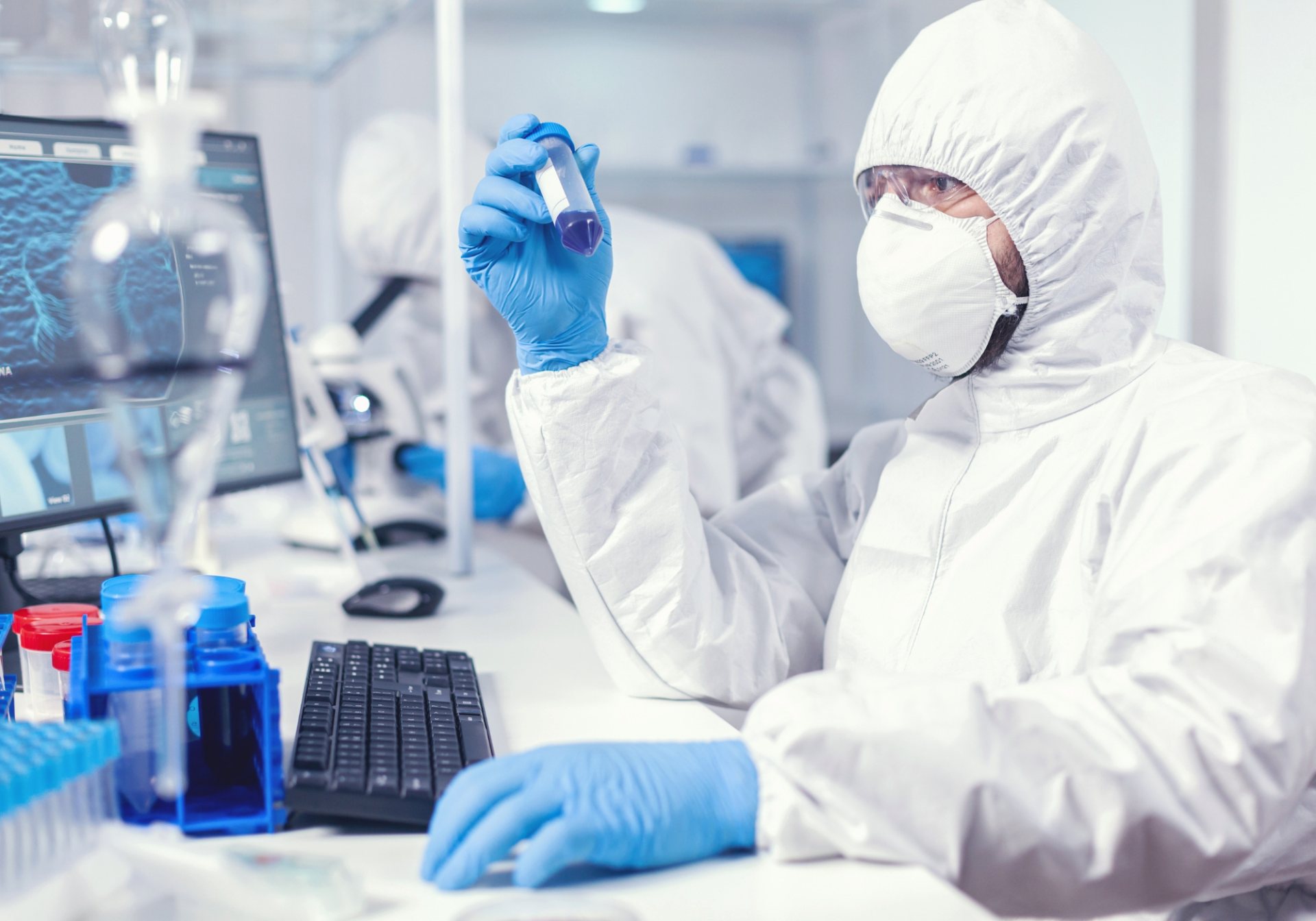 Scientist in protective coveralls inspecting a sample tube, the GMP records behind bioprocessing