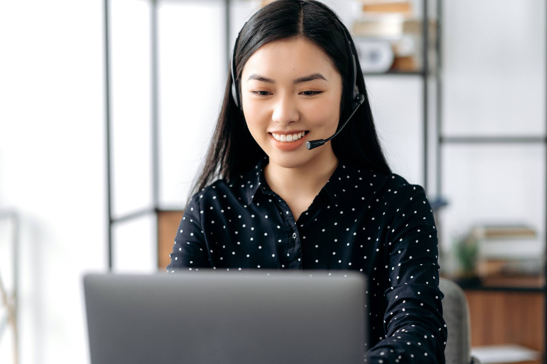 Call center agent with a headset helping a customer from her laptop on a busy voice queue