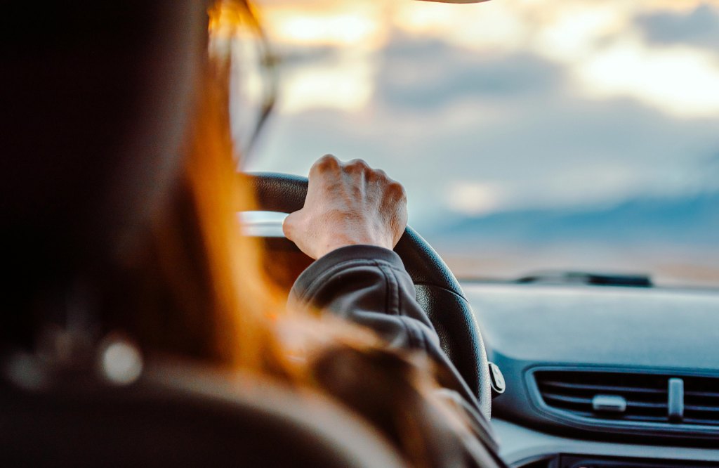 Driver with one hand on the steering wheel heading toward a sunset, representing car rental customer service outsourcing to the Philippines