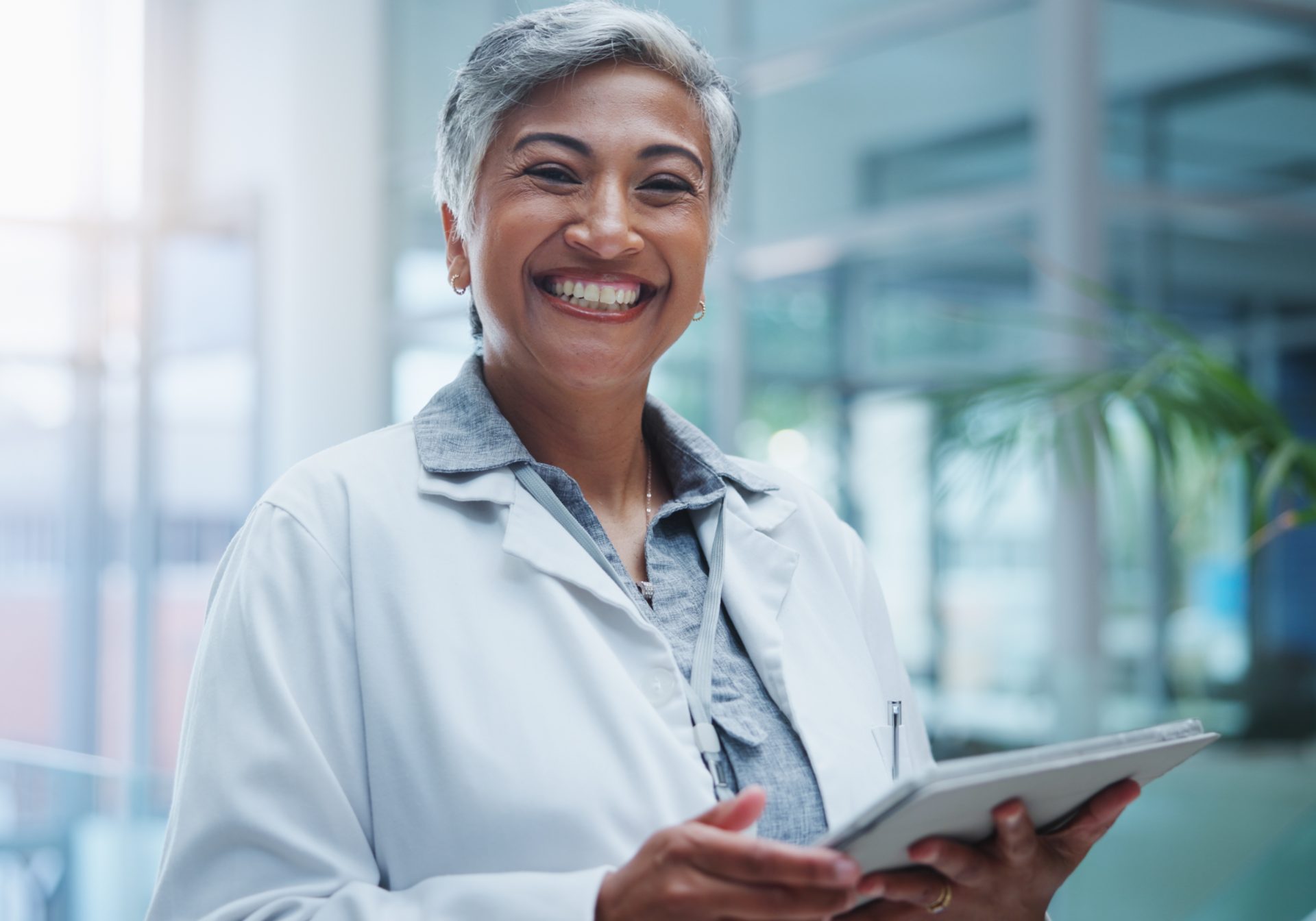 Smiling researcher in a lab coat holding a tablet, the site team clinical trial support works alongside