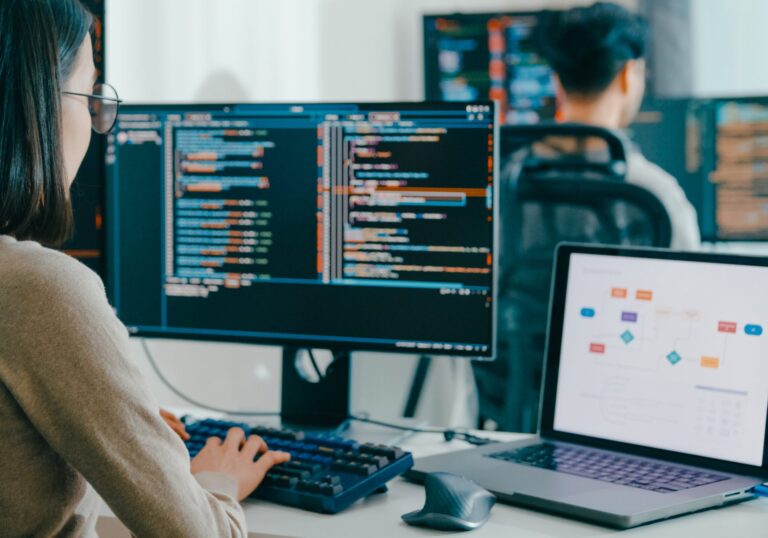 Developer reviewing code on a monitor with a flowchart on her laptop, for a post on screening developer annotators