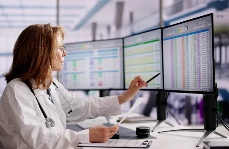 Physician reviewing claim and denial data across three monitors, for a post on common claim denial reasons