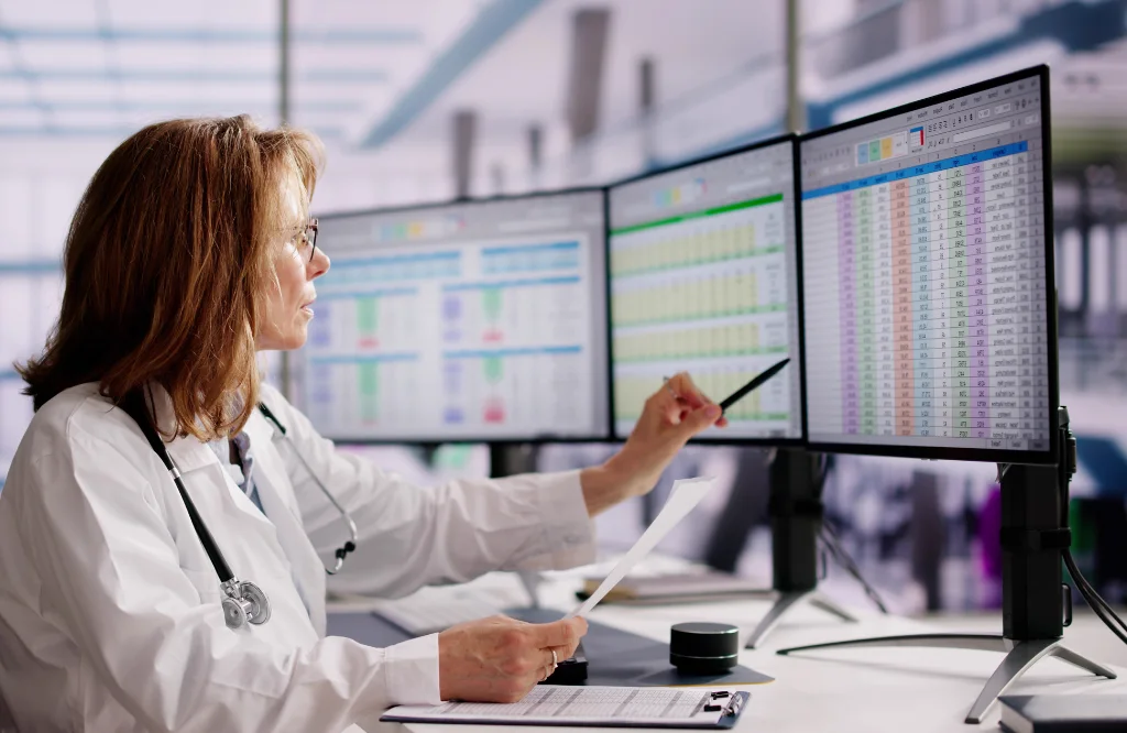 Physician reviewing claim and denial data across three monitors, for a post on common claim denial reasons