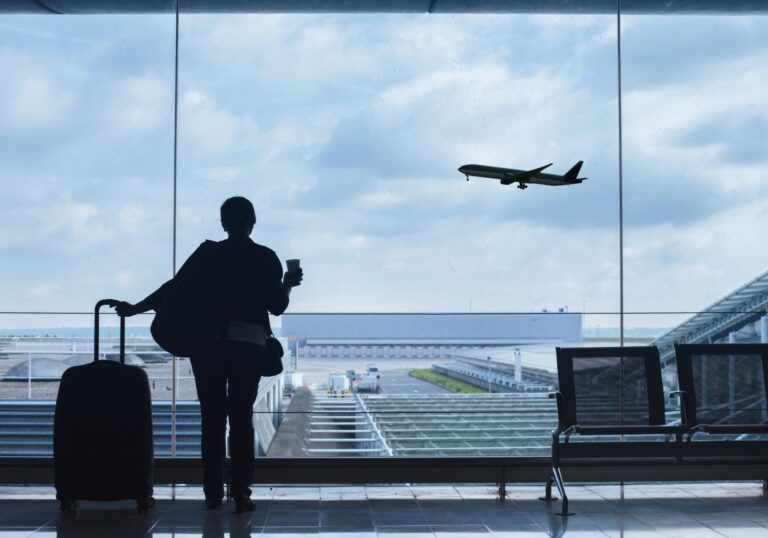 Traveler with a suitcase watching a plane take off from the terminal, for a post on duty of care business travel obligations