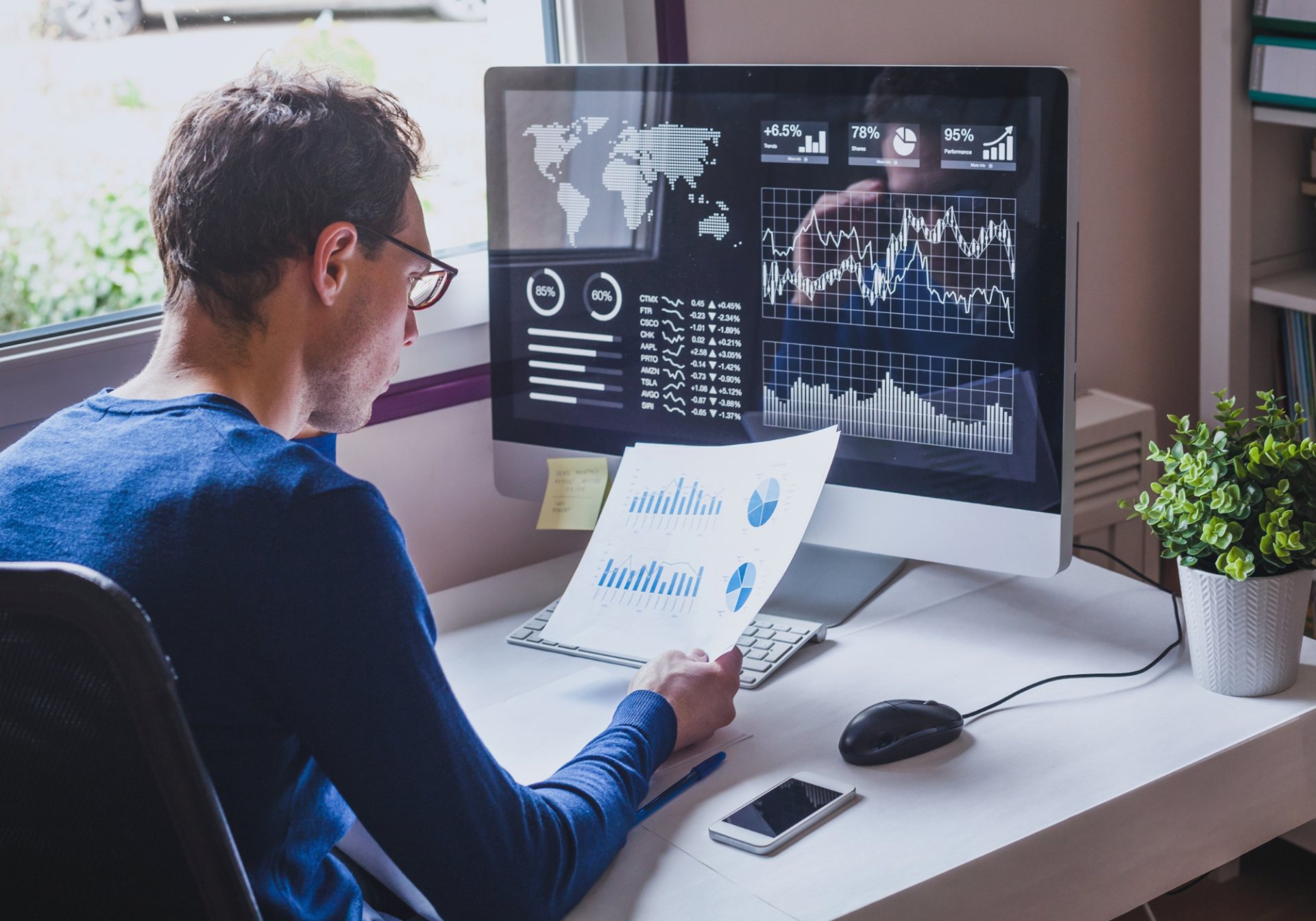 Analyst reviewing printed charts in front of a monitoring dashboard, watching for fraud and account abuse