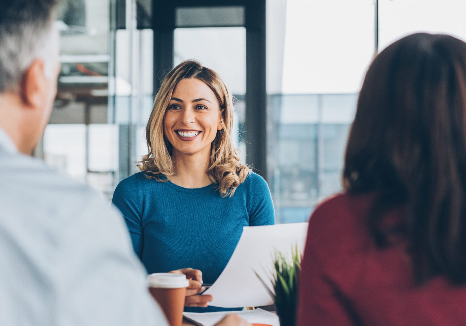 Smiling claims advisor taking first notice of loss from two policyholders across a table