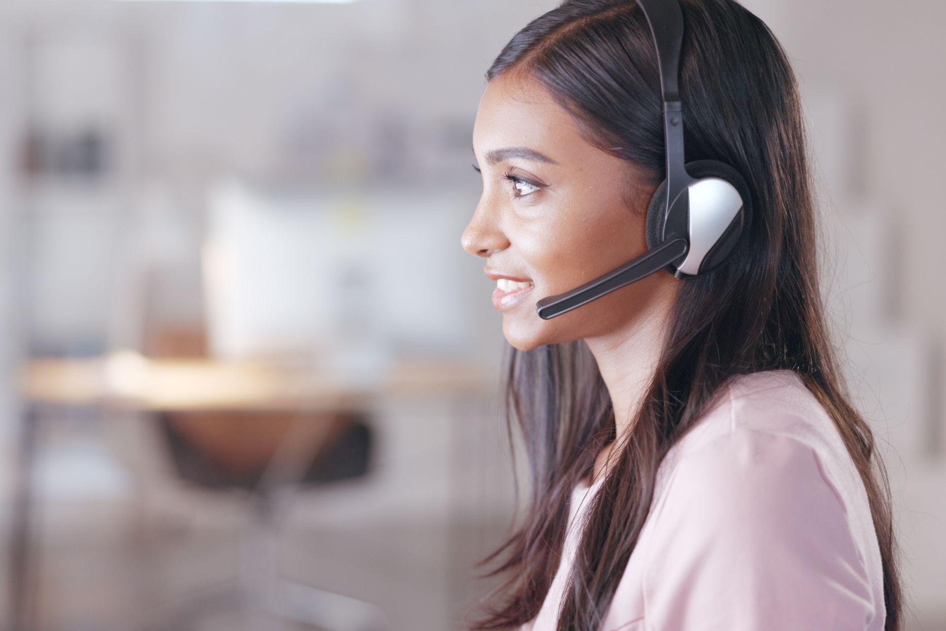 Filipino contact center agent in a headset looking toward her screen in a bright BPO office
