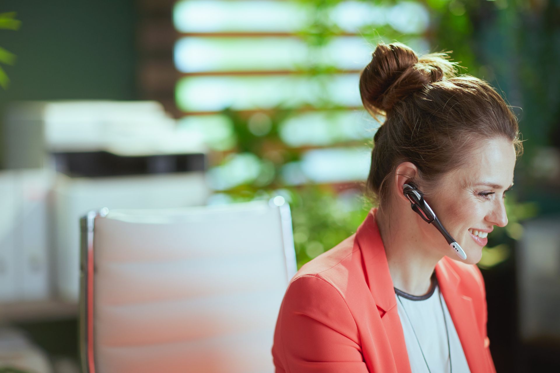 Smiling contact center agent in a red blazer wearing a headset at her desk in a modern Philippine office
