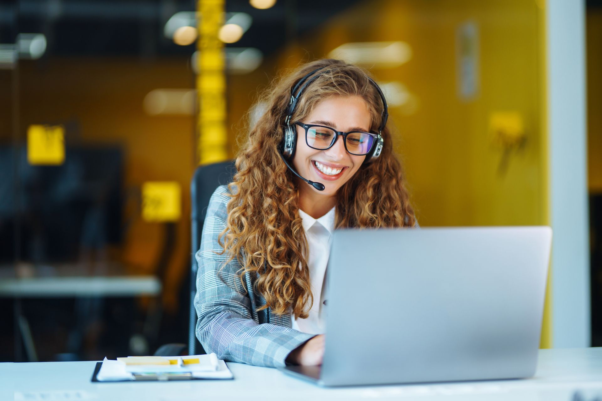 Smiling contact center agent in glasses and a headset working on a laptop in a modern Philippine BPO office