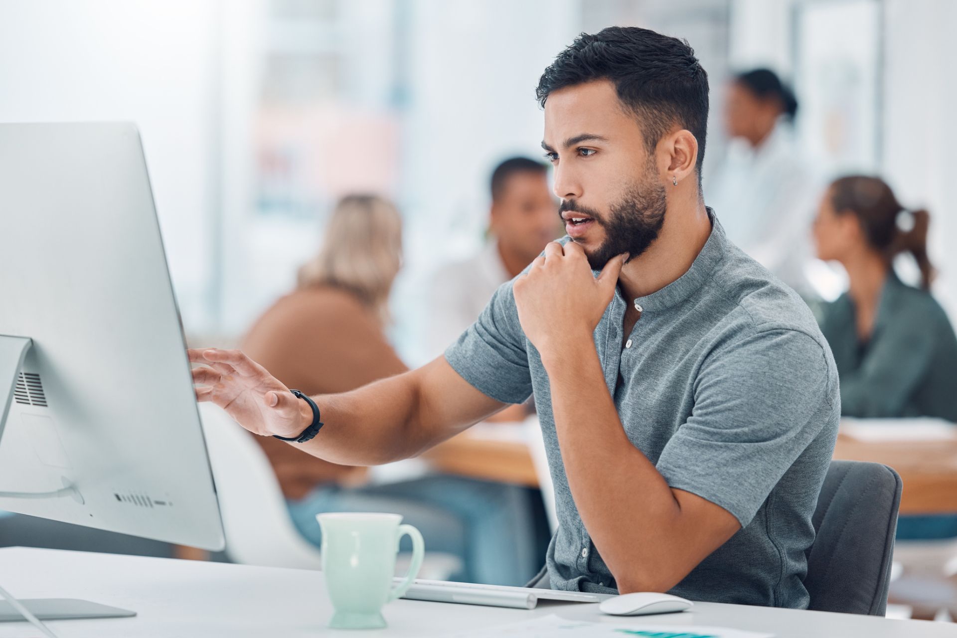 Analyst weighing outsourcing destinations on a desktop monitor in a busy modern office