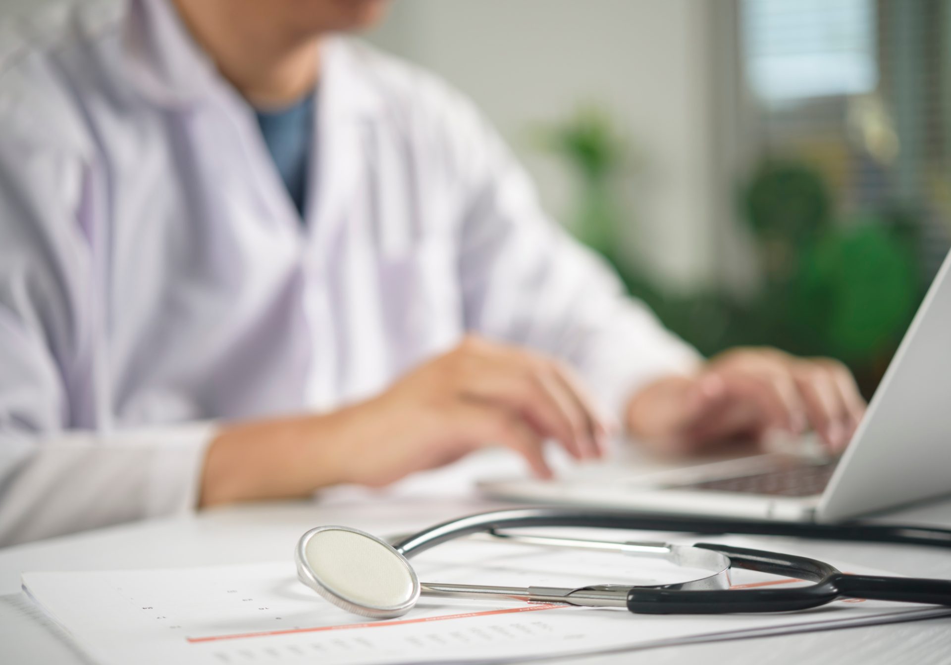 Clinician typing chart notes beside patient records, for a post on MEAT criteria risk adjustment
